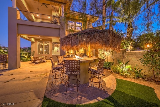 patio terrace at dusk featuring a balcony, exterior bar, and exterior kitchen