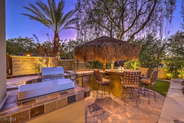 patio terrace at dusk featuring an outdoor bar, an outdoor kitchen, and area for grilling