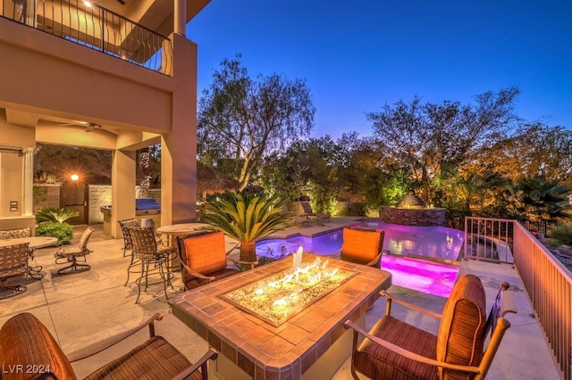 patio terrace at dusk with a fenced in pool, pool water feature, a balcony, ceiling fan, and an outdoor fire pit