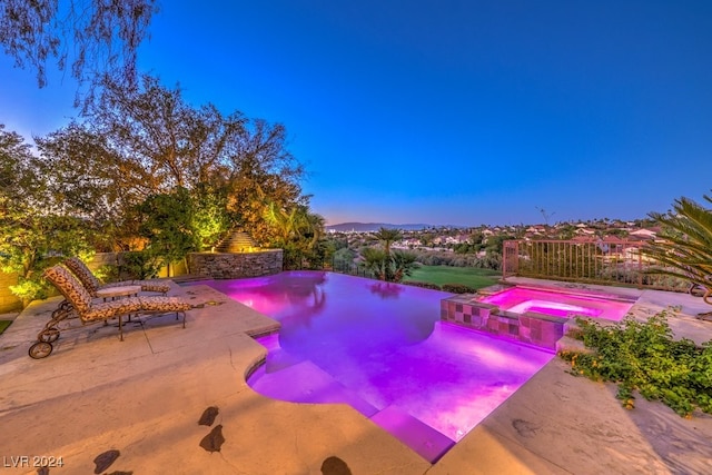 pool at dusk with an in ground hot tub and a patio