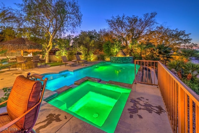 pool at dusk featuring an in ground hot tub, a patio area, and a bar