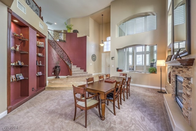 dining space with a towering ceiling, carpet, and a stone fireplace