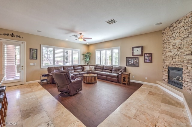 living room featuring ceiling fan, a textured ceiling, and a fireplace