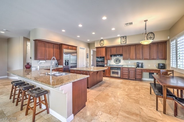 kitchen with pendant lighting, sink, kitchen peninsula, built in appliances, and a breakfast bar