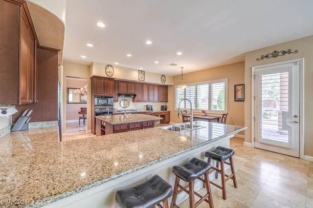 kitchen featuring an island with sink, hanging light fixtures, sink, a kitchen breakfast bar, and stainless steel microwave