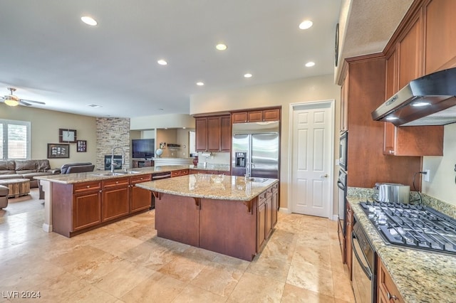 kitchen featuring a center island with sink, built in appliances, a kitchen breakfast bar, range hood, and light stone countertops