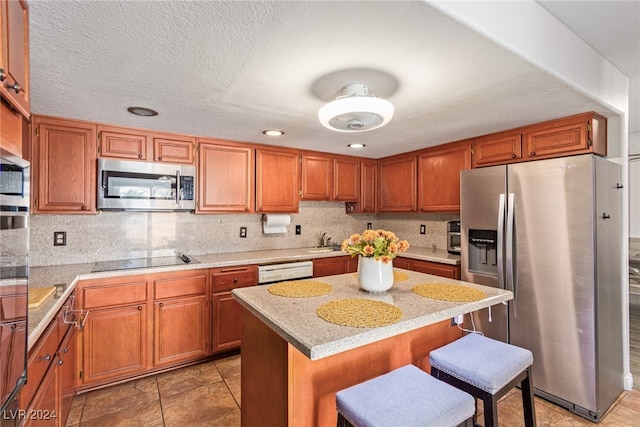 kitchen featuring a kitchen island, a breakfast bar, sink, appliances with stainless steel finishes, and a textured ceiling