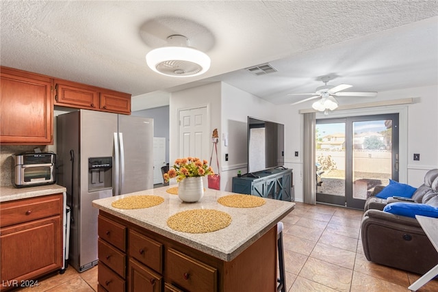 kitchen with ceiling fan, a kitchen island, stainless steel fridge, and a textured ceiling