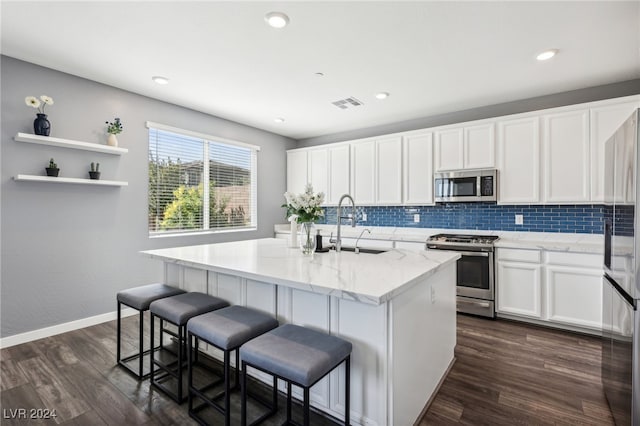 kitchen featuring white cabinets, an island with sink, appliances with stainless steel finishes, and dark wood-type flooring