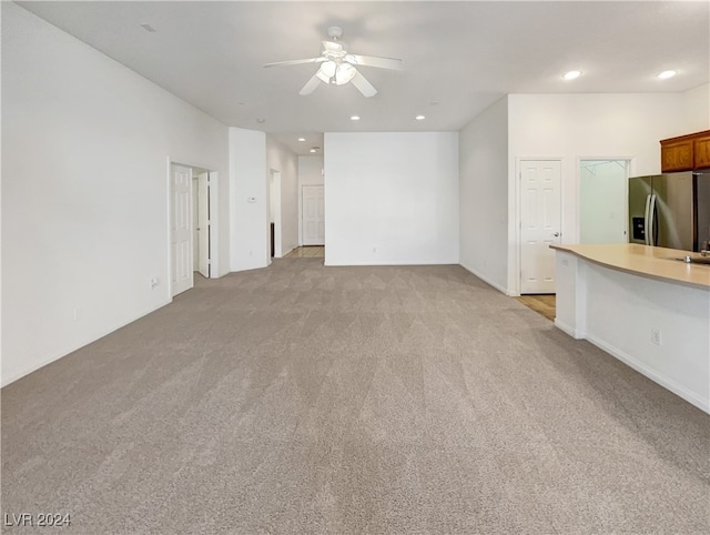 unfurnished living room with built in desk, light carpet, and ceiling fan