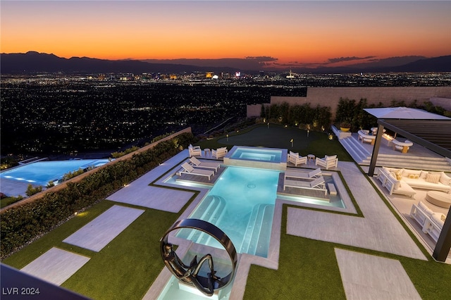 pool at dusk with a mountain view, an in ground hot tub, a patio area, and outdoor lounge area