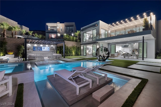 pool at night with a patio area and exterior kitchen