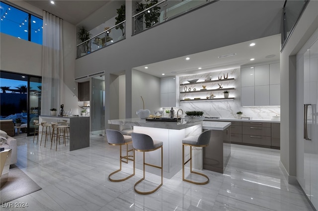 kitchen featuring a towering ceiling, an island with sink, tasteful backsplash, white cabinets, and a breakfast bar