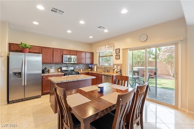 kitchen featuring decorative backsplash, light stone countertops, light tile patterned floors, a kitchen island, and stainless steel appliances