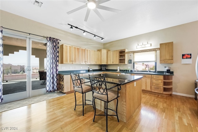 kitchen with a kitchen island, light hardwood / wood-style flooring, a kitchen breakfast bar, ceiling fan, and light brown cabinetry