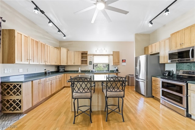 kitchen featuring appliances with stainless steel finishes, light hardwood / wood-style floors, a kitchen bar, a center island, and ceiling fan