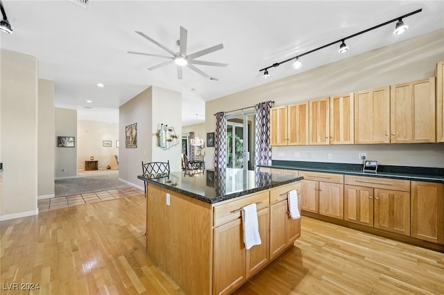 kitchen featuring ceiling fan, rail lighting, a center island, dark stone countertops, and light hardwood / wood-style floors