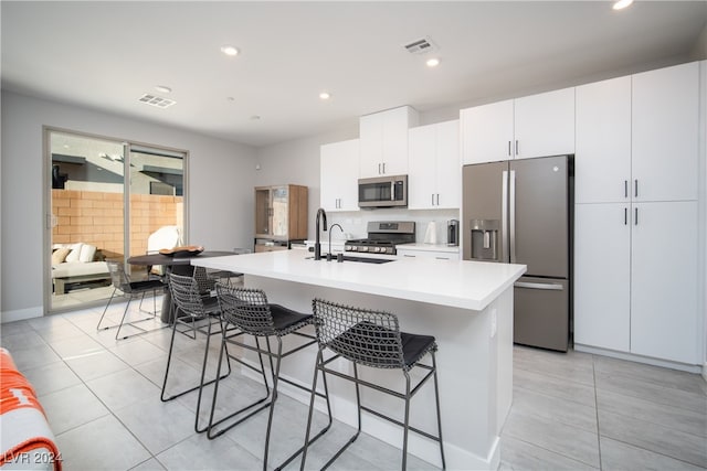 kitchen featuring an island with sink, white cabinetry, stainless steel appliances, a kitchen bar, and decorative backsplash