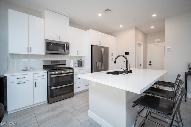 kitchen featuring white cabinets, sink, a center island with sink, appliances with stainless steel finishes, and a breakfast bar area