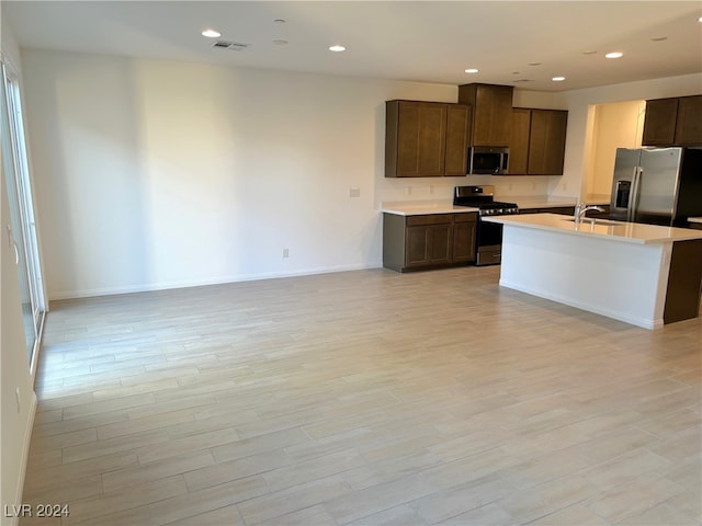 kitchen with a center island with sink, sink, light wood-type flooring, appliances with stainless steel finishes, and dark brown cabinets