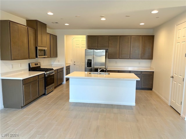 kitchen featuring sink, stainless steel appliances, dark brown cabinets, a center island with sink, and light wood-type flooring