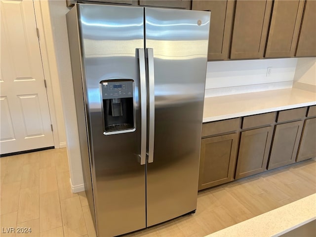 kitchen with dark brown cabinetry, stainless steel fridge with ice dispenser, and light wood-type flooring