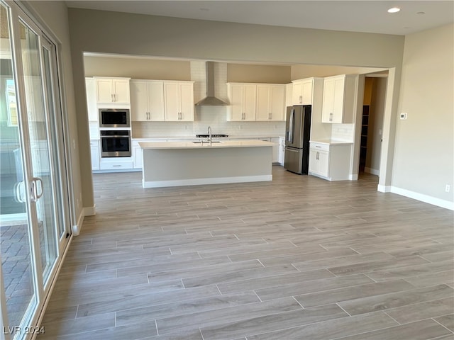 kitchen featuring a kitchen island with sink, light hardwood / wood-style flooring, wall chimney exhaust hood, appliances with stainless steel finishes, and white cabinetry