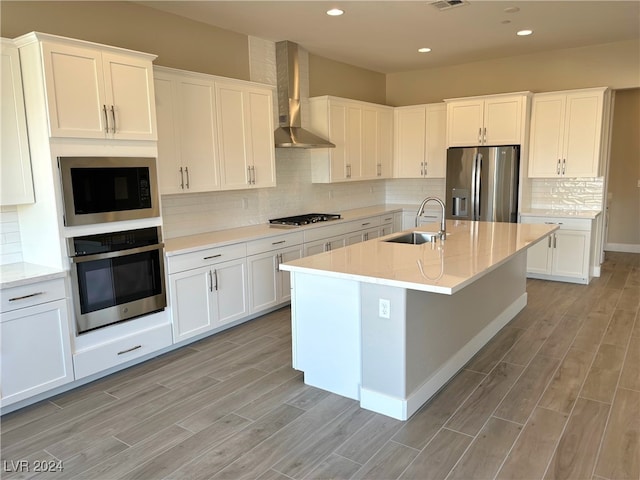 kitchen with appliances with stainless steel finishes, sink, white cabinetry, and wall chimney range hood