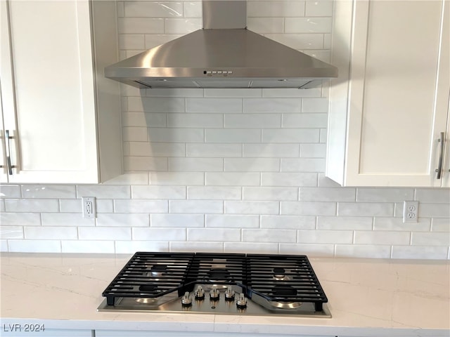 details with tasteful backsplash, white cabinets, light stone counters, and wall chimney exhaust hood