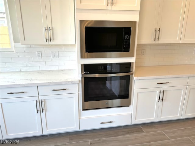 kitchen featuring light stone countertops, light wood-type flooring, stainless steel oven, built in microwave, and white cabinetry