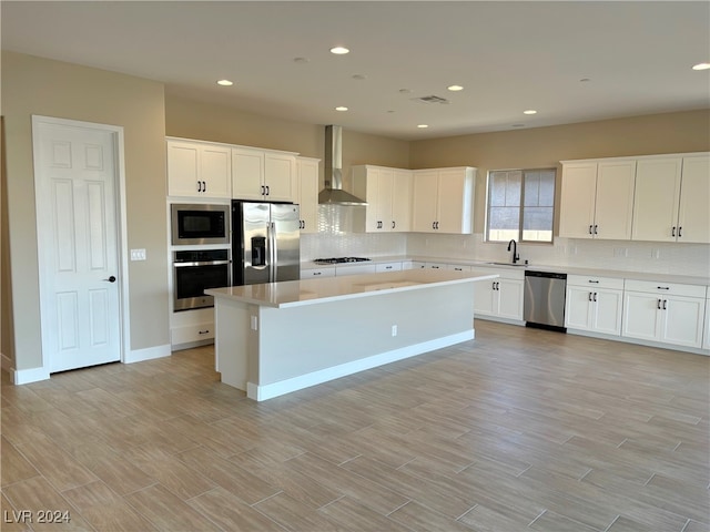 kitchen with wall chimney exhaust hood, stainless steel appliances, white cabinets, a center island, and light hardwood / wood-style floors