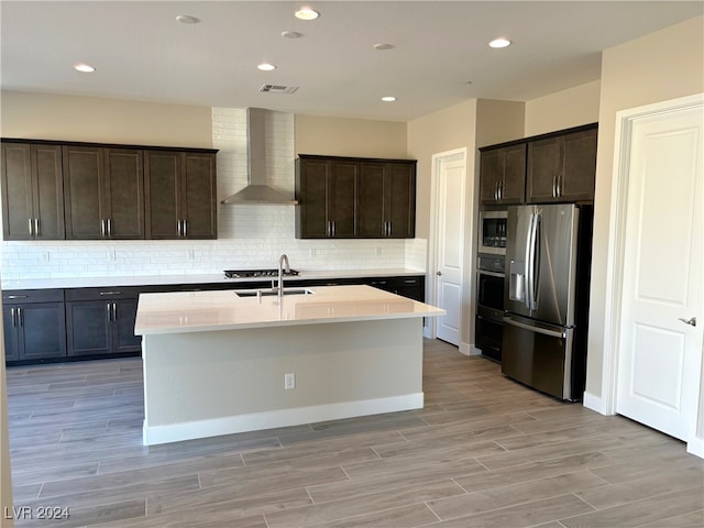 kitchen featuring a kitchen island with sink, dark brown cabinets, wall chimney range hood, and appliances with stainless steel finishes