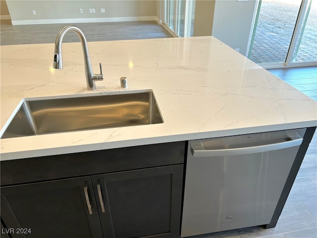 kitchen featuring light stone counters, light hardwood / wood-style floors, stainless steel dishwasher, and sink