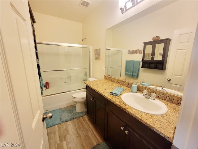 full bathroom with hardwood / wood-style floors, vanity, toilet, and bath / shower combo with glass door