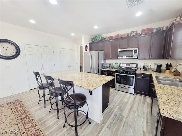 kitchen with sink, a kitchen island, light hardwood / wood-style flooring, appliances with stainless steel finishes, and a breakfast bar