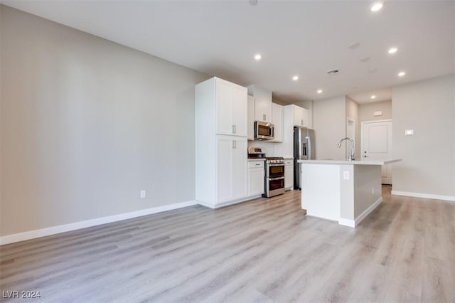 kitchen featuring an island with sink, light wood-type flooring, baseboards, and appliances with stainless steel finishes