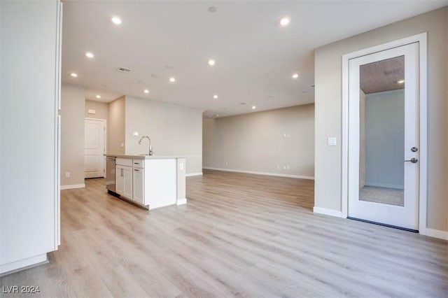 kitchen with white cabinets, light wood finished floors, a kitchen island with sink, a sink, and open floor plan