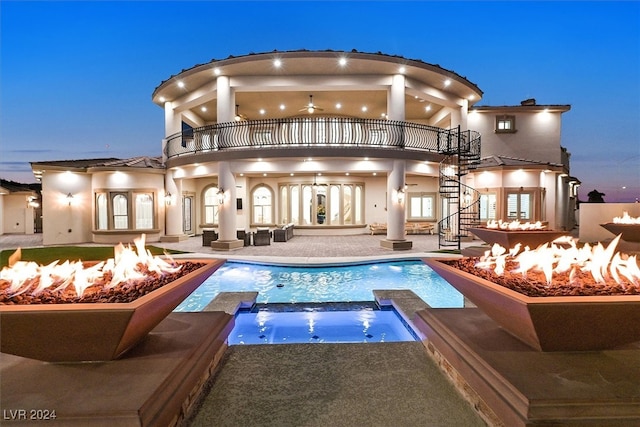 back house at dusk featuring a balcony, an outdoor fire pit, a patio area, a swimming pool with hot tub, and pool water feature