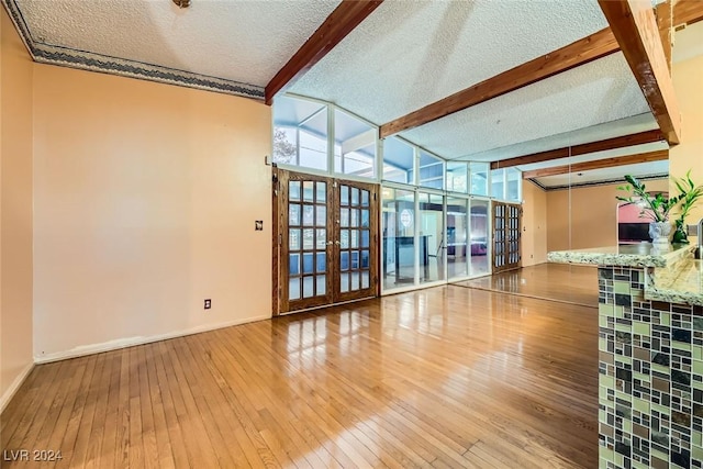 unfurnished living room featuring french doors, beamed ceiling, a textured ceiling, and hardwood / wood-style flooring