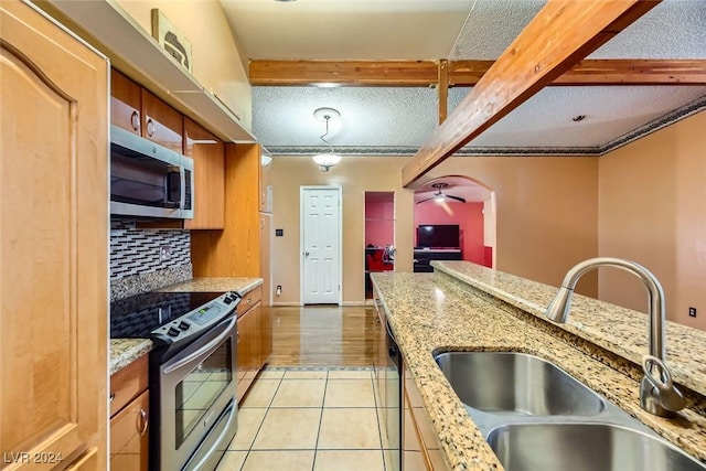 kitchen with appliances with stainless steel finishes, a textured ceiling, sink, beam ceiling, and light hardwood / wood-style floors