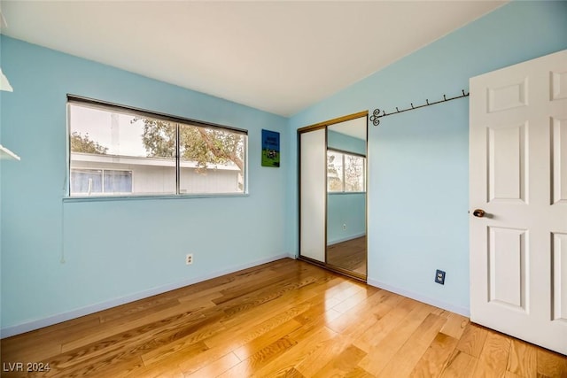 unfurnished bedroom featuring light hardwood / wood-style floors, a closet, and lofted ceiling