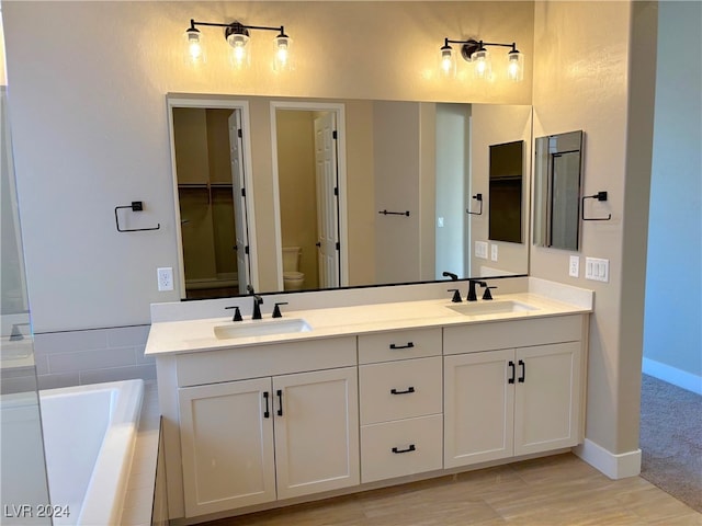 bathroom with tiled bath, vanity, and toilet