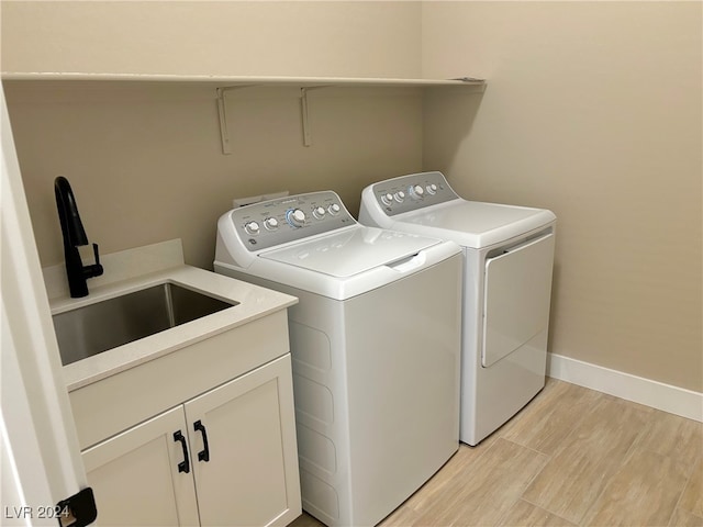 clothes washing area with light hardwood / wood-style floors, cabinets, separate washer and dryer, and sink