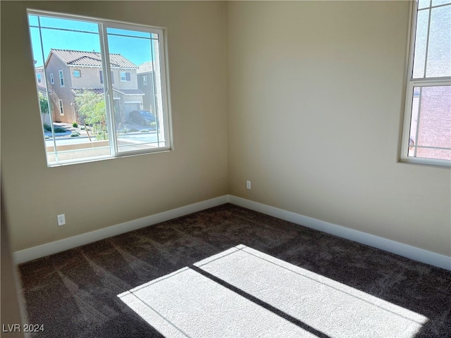 empty room with dark colored carpet and a wealth of natural light