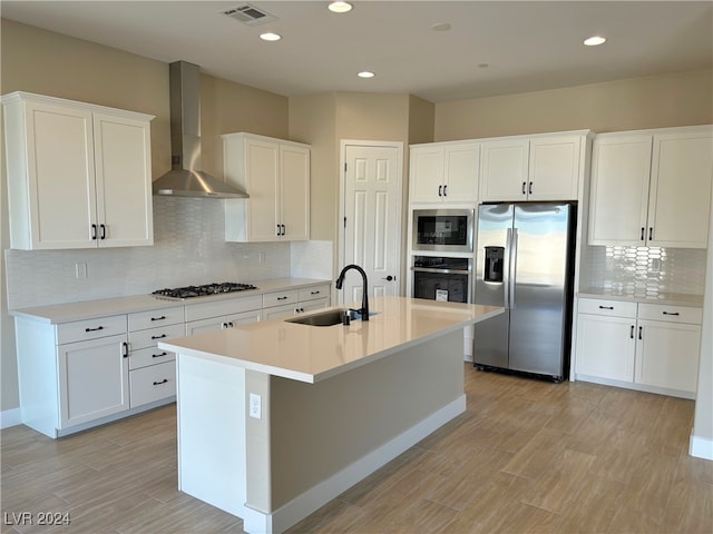 kitchen with white cabinetry, sink, wall chimney range hood, an island with sink, and appliances with stainless steel finishes