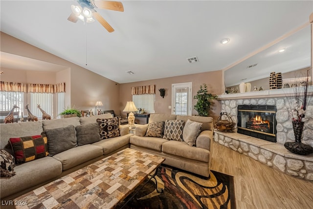 living room featuring vaulted ceiling, ceiling fan, hardwood / wood-style floors, and a stone fireplace