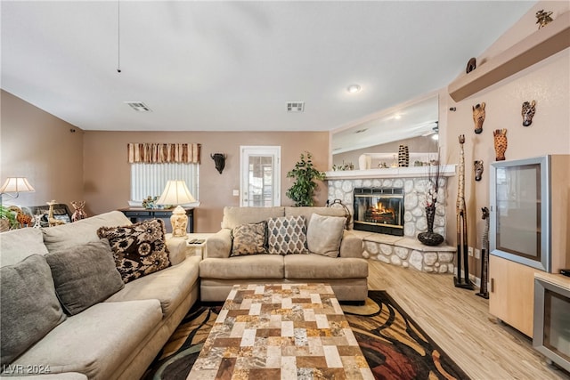 living room with light hardwood / wood-style flooring, vaulted ceiling, and a stone fireplace