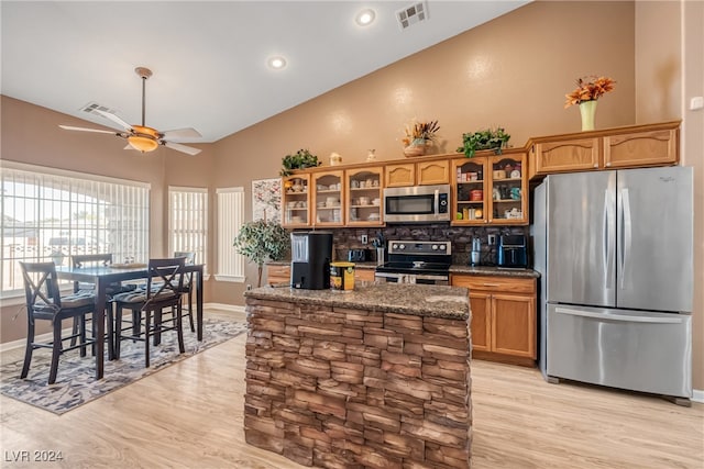 kitchen featuring appliances with stainless steel finishes, tasteful backsplash, ceiling fan, light hardwood / wood-style flooring, and dark stone counters