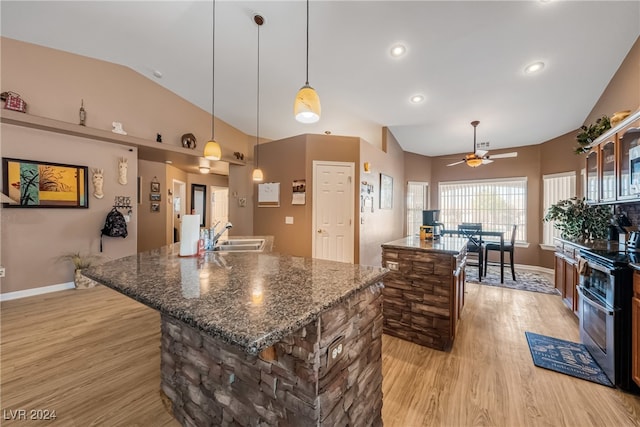 kitchen featuring ceiling fan, a kitchen island, dark stone counters, stainless steel range oven, and light wood-type flooring