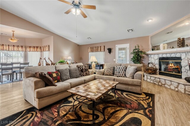 living room featuring ceiling fan, a stone fireplace, lofted ceiling, and light hardwood / wood-style floors